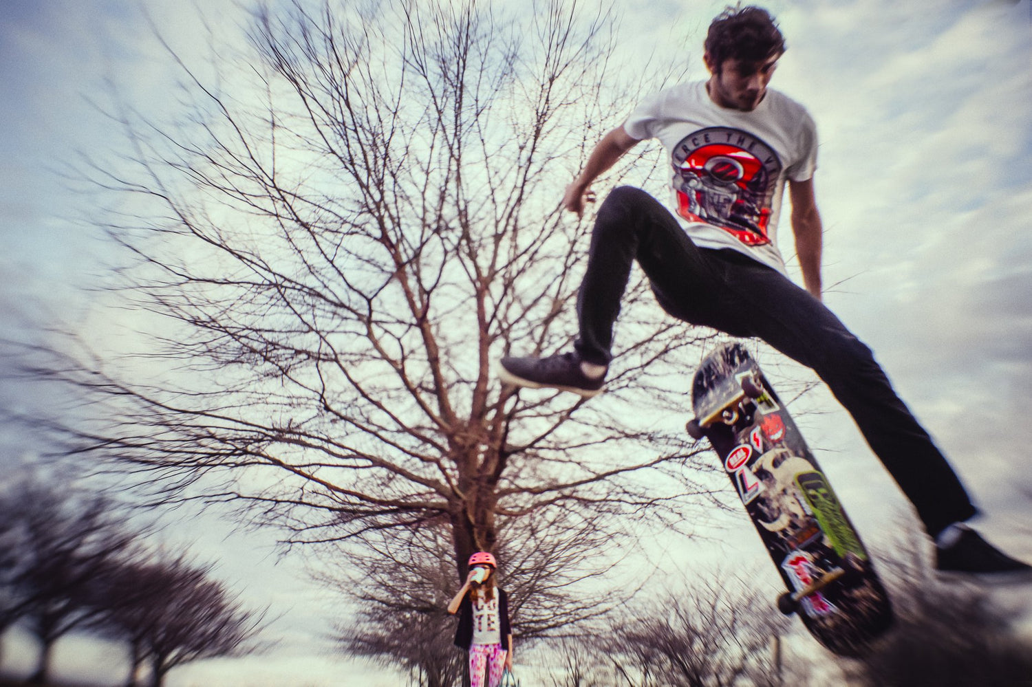 skateboarder kickflip ollie jump man in jeans and white t-shirt during winter while girl in pink helmet watches featured photos