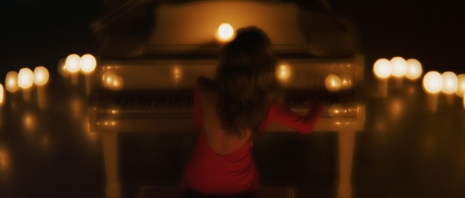 blonde woman in red dress plays the piano in a candlelit room moonlight skyfall music video velvet 56